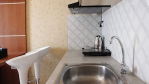 A kitchen with a stainless steel sink, a kettle, and a wooden cabinet.