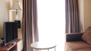 A hotel room with a flat-screen TV, a lamp, a small round table, and a brown sofa.