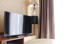 A hotel room with a flat-screen TV on a wooden stand, a lamp, and a round wooden table.