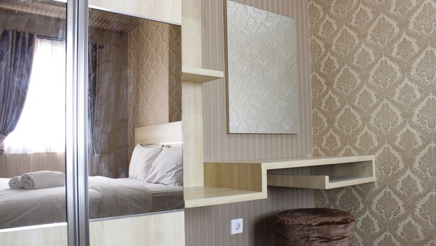 A modern hotel room with a bed, a vanity with a mirror, a wooden shelf, and a patterned wallpaper.