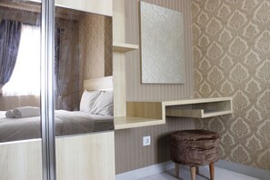 A modern hotel room with a bed, a vanity with a mirror, a wooden shelf, and a patterned wallpaper. - Classic 2BR Apartment at Mekarwangi Square Cibaduyut (Bandung)