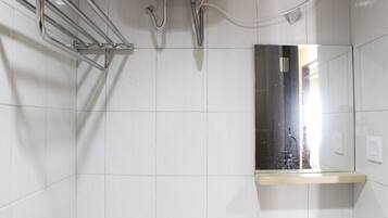 Une salle de bain avec des murs carrelés de carreaux blancs, un porte-serviettes en métal, un miroir et une étagère en bois.
