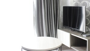 A modern room with a TV on a stand, a round table, and a curtain. - Modern 2BR Apartment at Mekarwangi Square Cibaduyut (Bandung)