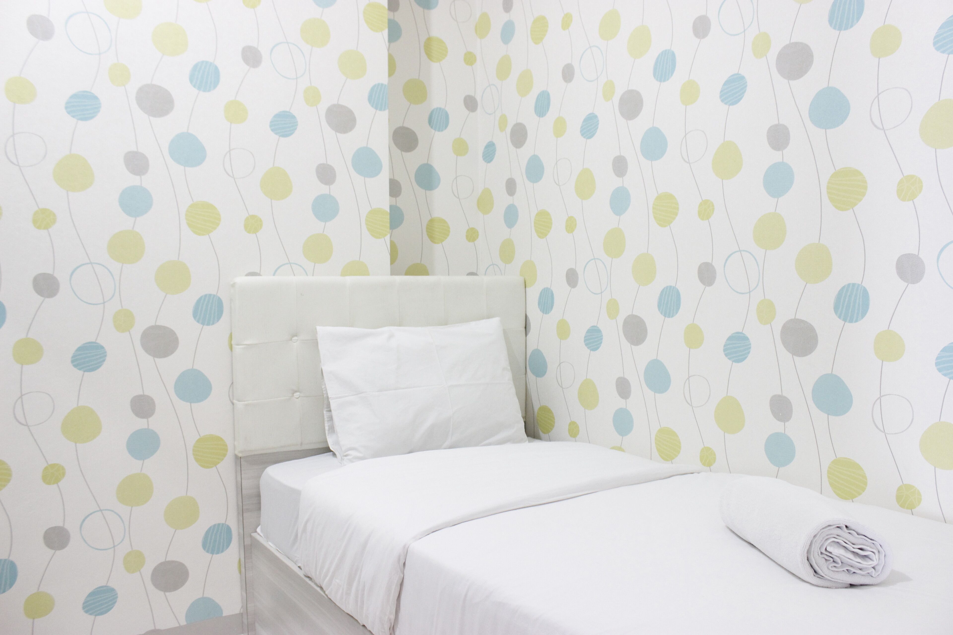 A neatly made bed with white bedding, a white pillow, and a rolled white towel on the right side.