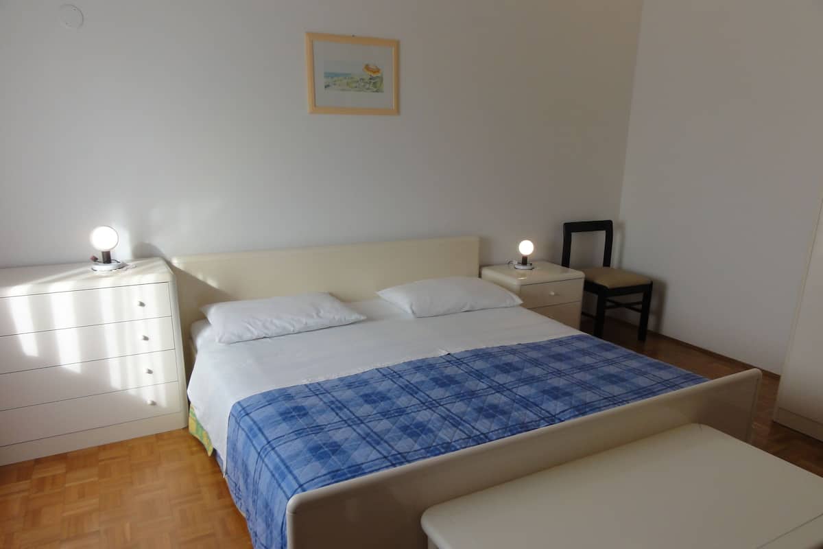 Quarto com cama, mesas de cabeceira, uma cadeira e uma mesinha.