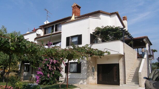 A two-story house with a stone-paved driveway, a garden with flowering plants, and a parked car. - Nice and Cozy Apartment Ferry in Medulin (Medulin)