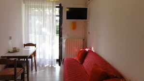 A room with a dining table, chairs, a red sofa, a TV mounted on the wall, and an air conditioning unit. - Nice and Cozy Apartment Ferry in Medulin (Medulin)
