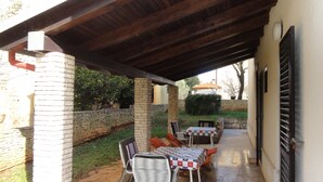 An outdoor patio with a covered seating area, stone walls, and a view of the garden. - Nice and Cozy Apartment Ferry in Medulin (Medulin)