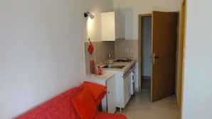 A compact kitchen with a sink, stove, and cabinets, a red sofa, and a door leading to another room. - Nice and Cozy Apartment Ferry in Medulin (Medulin)