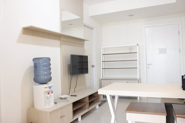 Une pièce moderne équipée d’un bureau blanc, d’un téléviseur à écran plat, d’un distributeur d’eau et d’un tableau blanc mural.