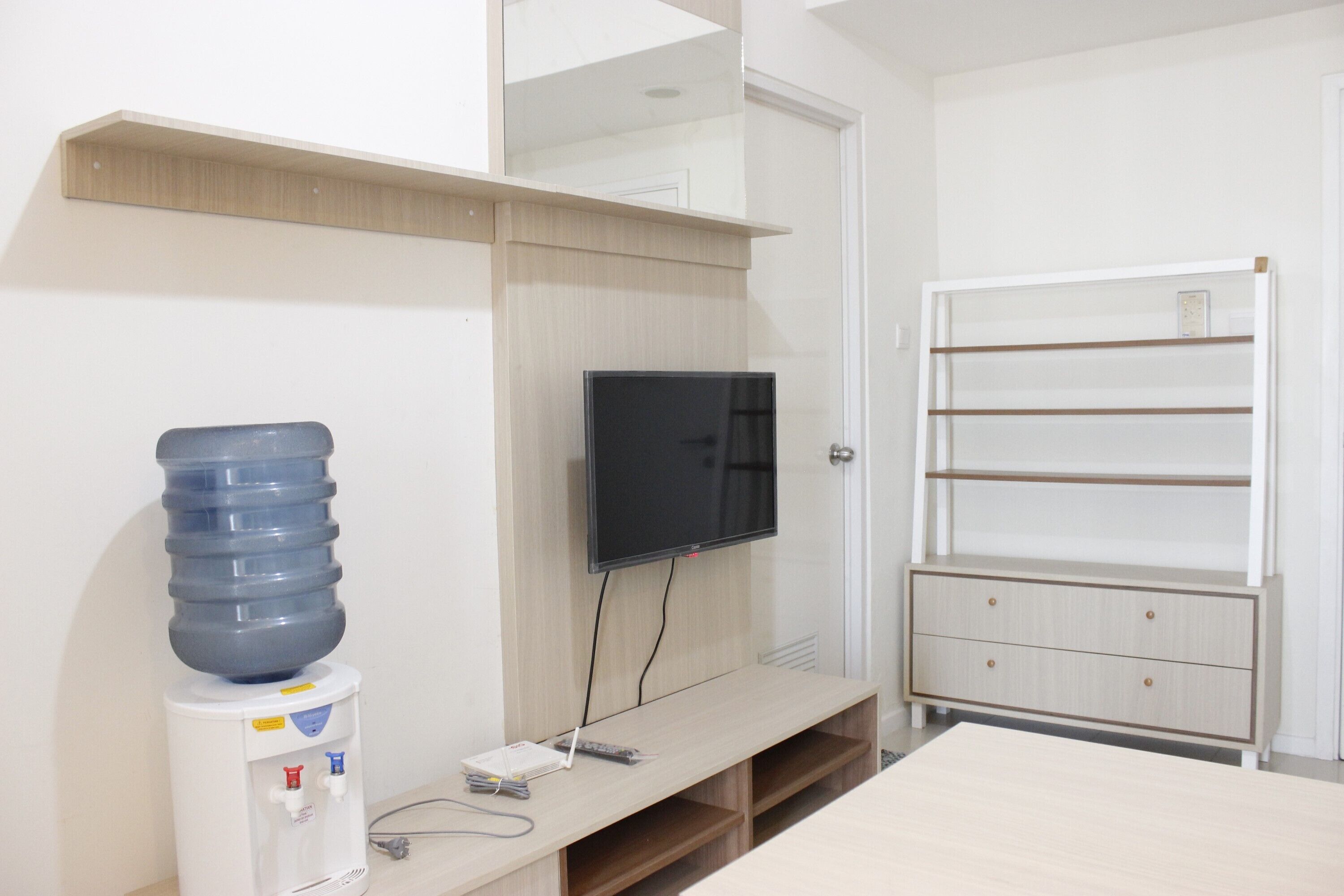Een hotelkamer met een flatscreen televisie aan de wand, een waterdispenser, een houten kast met lades en een bed.