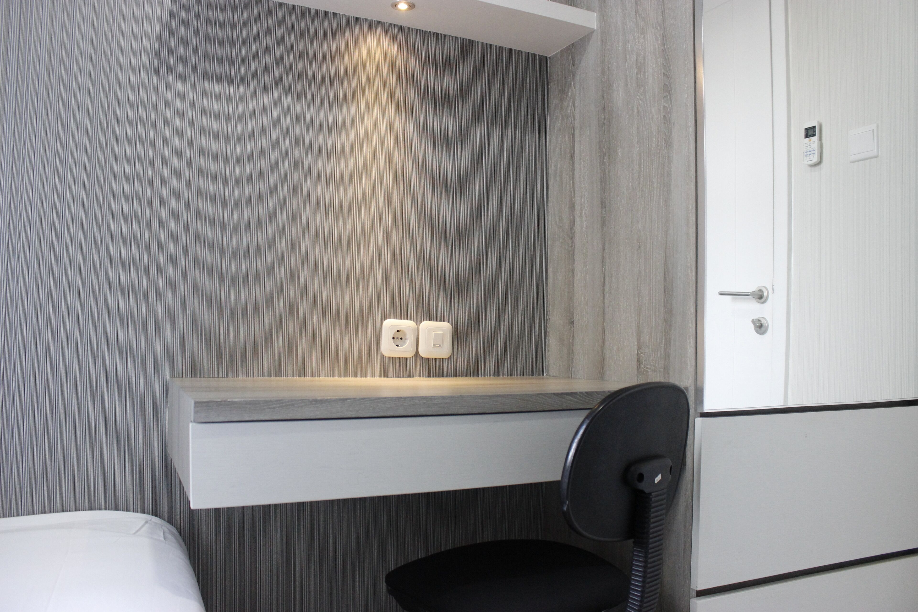A modern bathroom with a grey striped wall, a white vanity with a mirror, and a black chair.