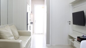 A modern hotel room with a white sofa, a flat-screen TV mounted on the wall, and a door leading to another room.