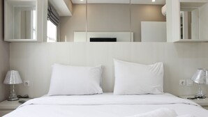 A modern hotel room with a large bed, white bedding, two bedside lamps, and a flat-screen TV mounted on the wall.