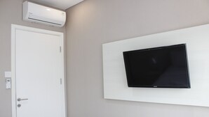 A room with a mounted flat-screen TV on a white wall, a white door with a handle, and an air conditioning unit above the door.