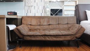 Une chambre moderne avec un canapé marron, un lit et un petit bureau sur lequel se trouve un ordinateur portable.