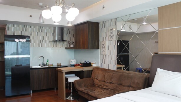 Une chambre d’hôtel moderne dotée d’une kitchenette, d’un canapé en cuir marron, d’un lit avec une literie blanche et d’un décor mural géométrique original.