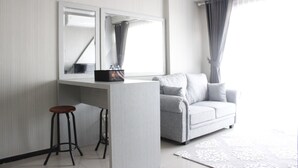 A modern living room with a grey sofa, a white desk with a mirror, and a bar stool. - Stylish 2BR Gateway Pasteur Apartment (Cimahi)