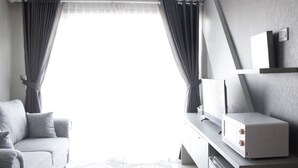 A modern living room with a grey sofa, a flat-screen TV, and a microwave on a wooden cabinet. - Stylish 2BR Gateway Pasteur Apartment (Cimahi)