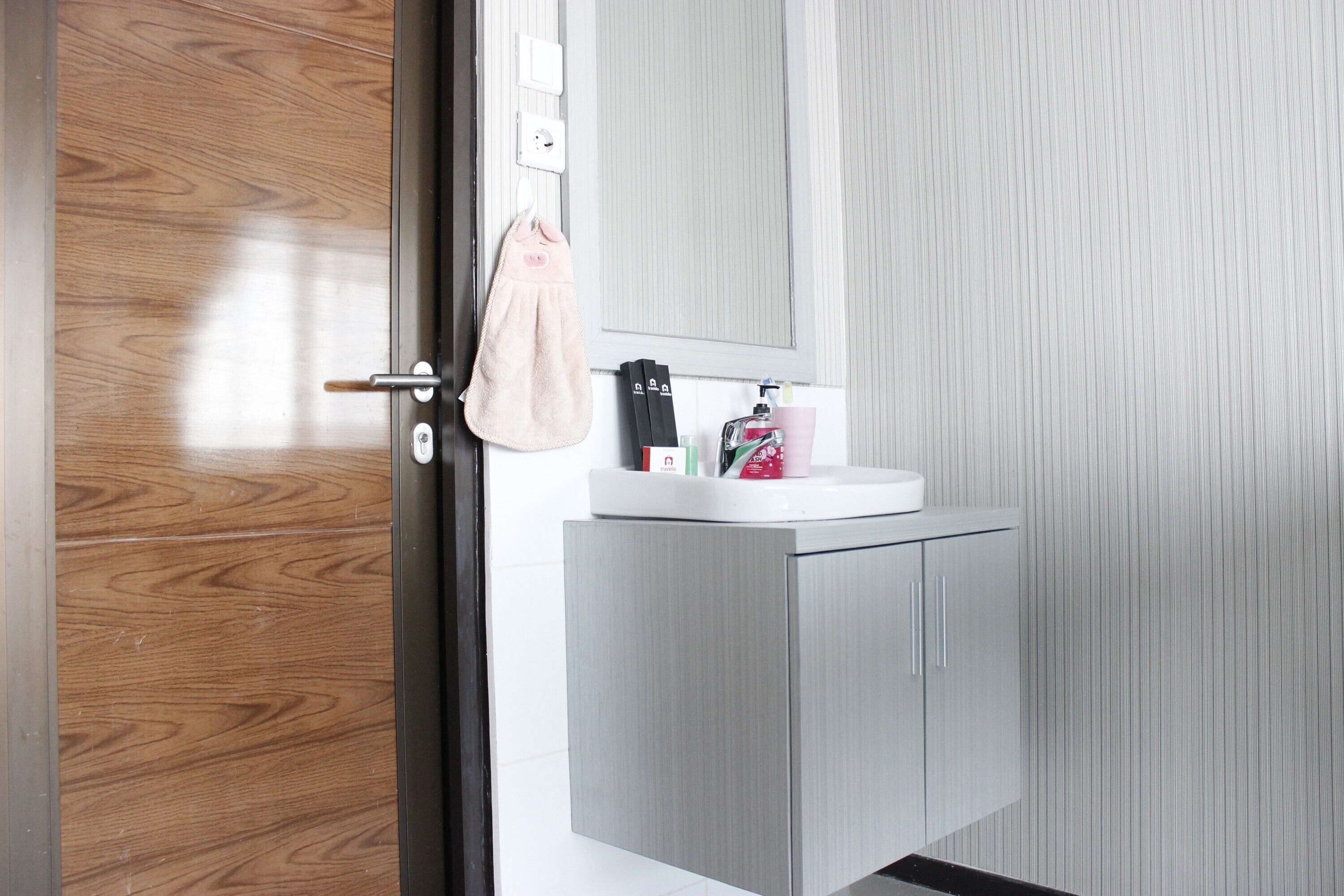 Een moderne badkamer met een houten deur, een witte wastafel en een spiegel erboven.