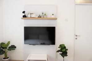 Une pièce avec un téléviseur fixé au mur, une petite table blanche et deux plantes en pot.