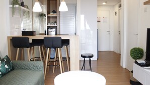 A modern living room with a sofa, a round coffee table, and a kitchen area with bar stools. - Classic and Comfy 2BR @ Gateway Pasteur Apartment (Cimahi)