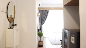 A hallway with a white refrigerator, a mirror, a small potted plant, and a black refrigerator. - Classic and Comfy 2BR @ Gateway Pasteur Apartment (Cimahi)
