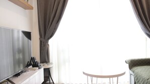 A modern living room with a flat-screen TV, a small round table, and a sofa. - Classic and Comfy 2BR @ Gateway Pasteur Apartment (Cimahi)