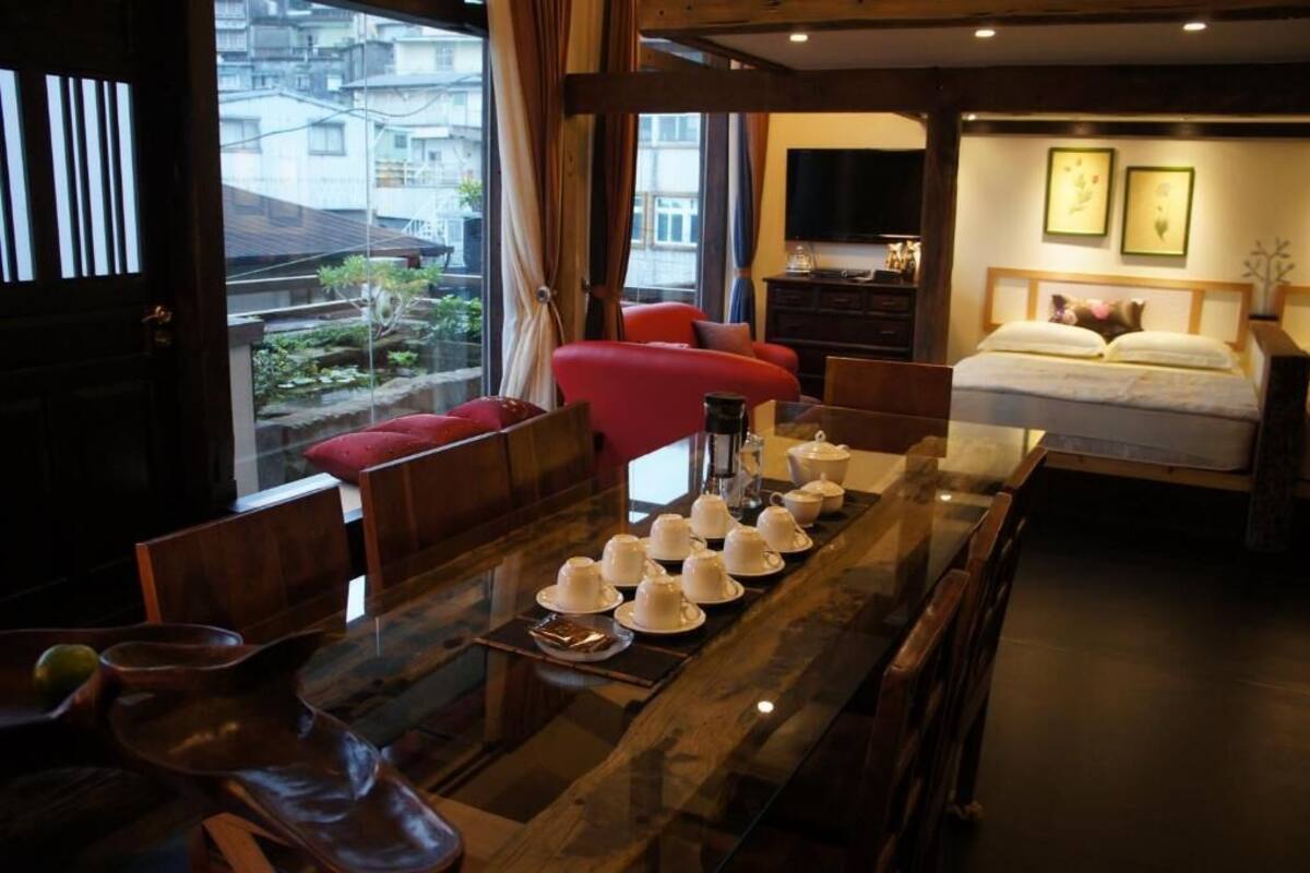 Une chambre d’hôtel avec une table à manger mise, des tasses à thé disposées dessus, un lit recouvert d’une couette blanche et un téléviseur fixé au mur.