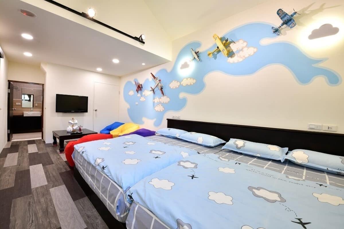 Une chambre d’hôtel avec deux lits, une télévision et une fresque murale représentant des avions.