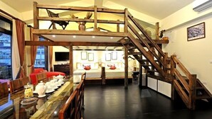 A room with a loft bed, a wooden staircase, a dining table with teapots, and a view of the outside.