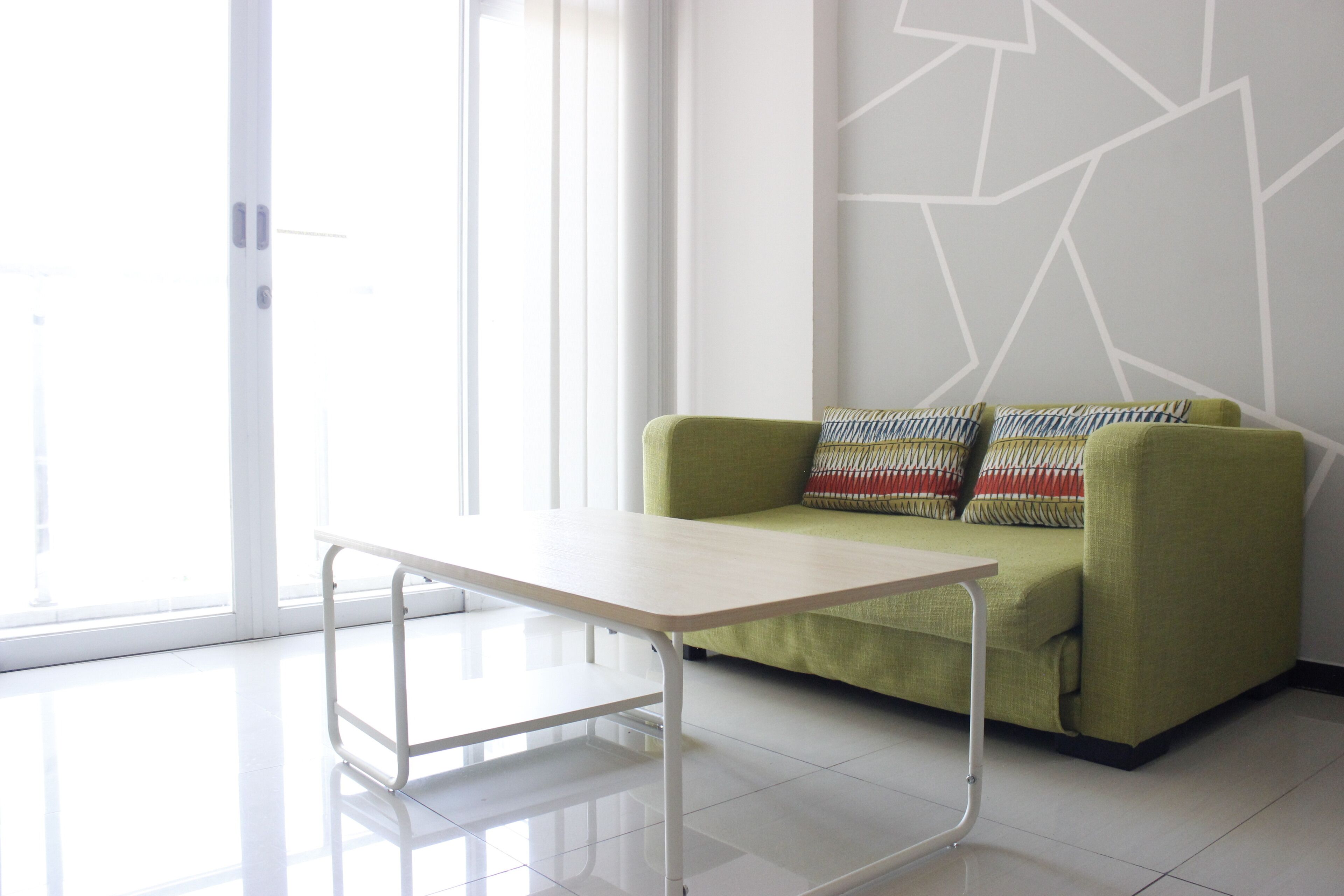 Una habitación moderna con un sofá verde, una mesa blanca y un diseño geométrico en la pared.