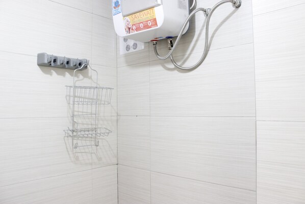 A bathroom with white tiled walls, a shower with a hose, and a metal rack for hanging items.