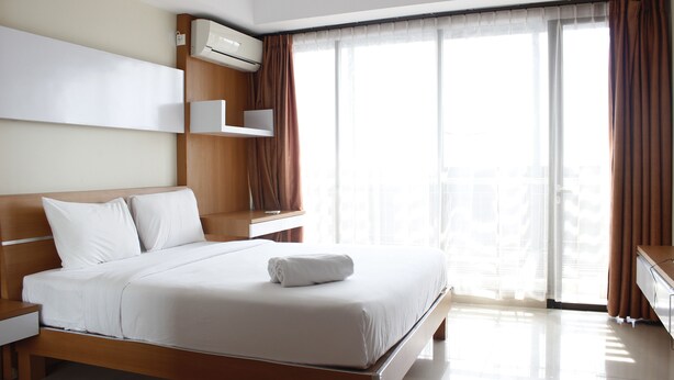 Una habitación de hotel moderna con una cama grande, aire acondicionado integrado y vistas a la ciudad a través de amplios ventanales.