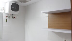 Un baño con paredes de azulejos blancos, un estante blanco, un inodoro blanco y un calentador de agua montado en la pared.