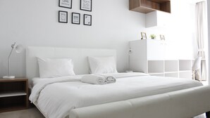 Ein modernes Schlafzimmer mit einem großen Bett, weißer Bettwäsche, einem Nachttisch mit Lampe, einem Kleiderschrank und Wandbildern.
