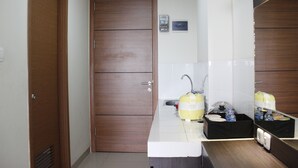 Un baño de hotel pequeño con puerta de madera, un lavabo con espejo y una pequeña encimera con artículos de aseo.