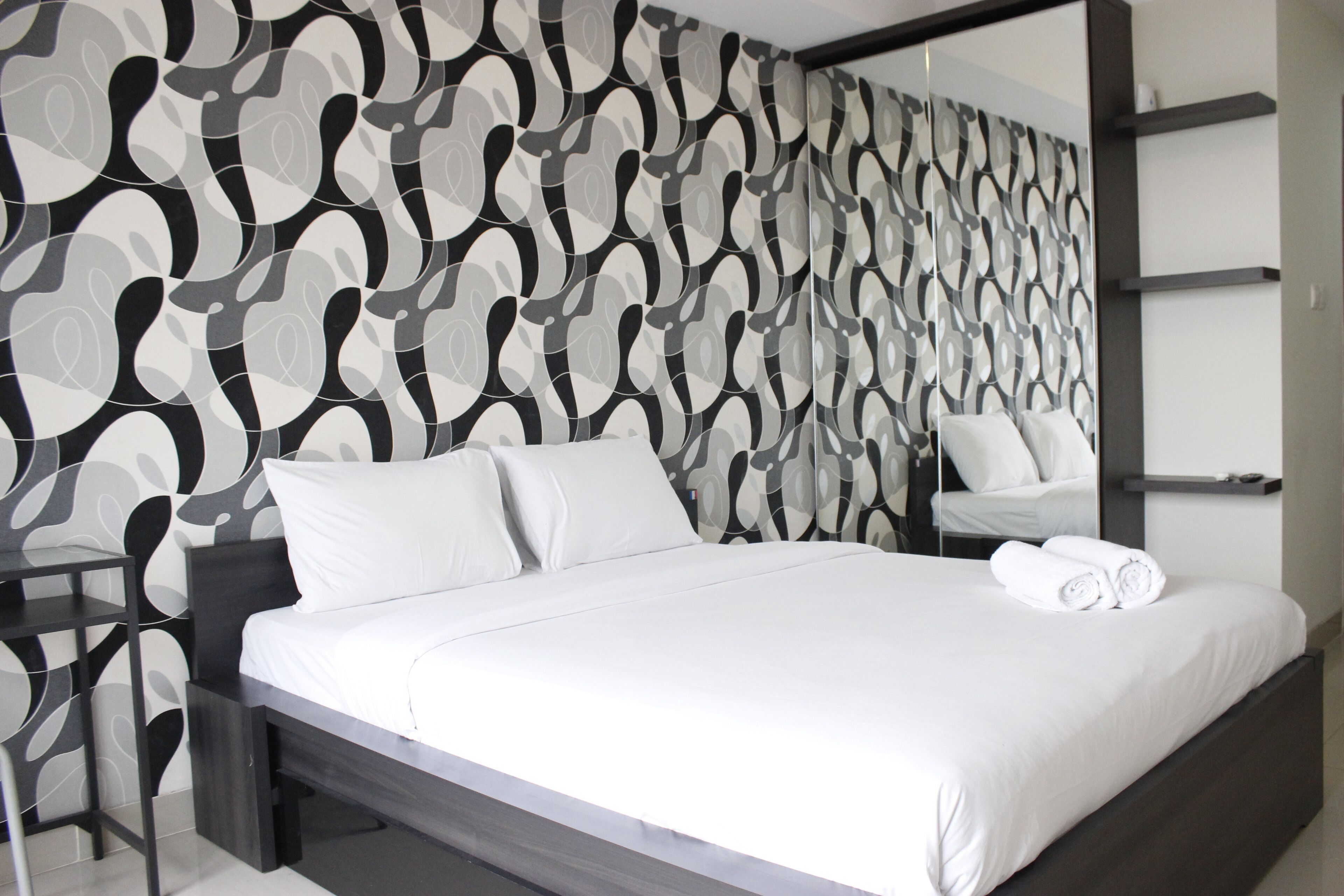 Un dormitorio moderno con cama, ropa de cama blanca, una mesita de noche y un espejo.