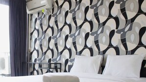 Habitación de hotel con cama, ropa de cama blanca, pared con diseño y un equipo de aire acondicionado.