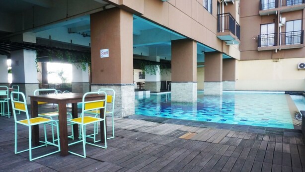 An outdoor pool area with a wooden deck, metal chairs, and a sign indicating no smoking. - Cozy 2BR Tamansari Panoramic Apartment (Bandung)