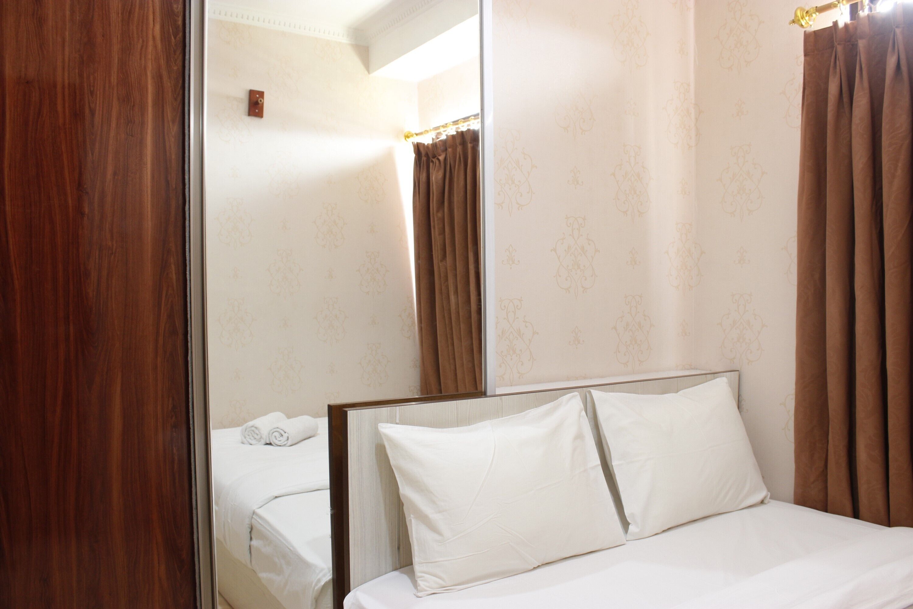 Una habitación de hotel con un espejo grande, una cama con ropa blanca y cortinas marrones.
