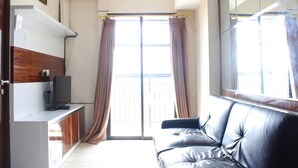 A room with a leather sofa, a television on a stand, a sliding glass door, and a wooden cabinet. - Cozy 2BR Tamansari Panoramic Apartment (Bandung)