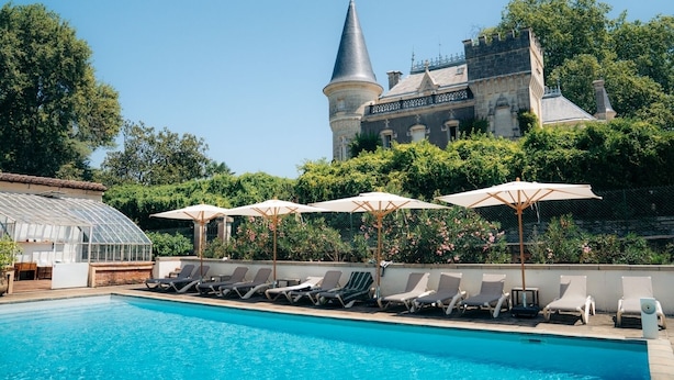 A pool area with lounge chairs and umbrellas, a greenhouse, and a castle-like building in the background. - Holiday rental 5 personnes Château Belle Epoque Landes (Linxe)