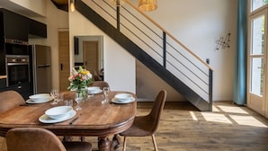 A dining area with a wooden table, chairs, and a staircase with a railing. - Holiday rental 5 personnes Château Belle Epoque Landes (Linxe)