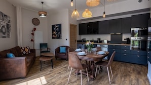 A modern kitchen with dark cabinets, a built-in oven, and a dining area with a wooden table and chairs. - Holiday rental 5 personnes Château Belle Epoque Landes (Linxe)