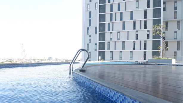 A swimming pool with a tiled edge and a metal handrail, surrounded by a wooden deck. - 2BR Apartment near Marvell City Mall at The Linden (Surabaya)