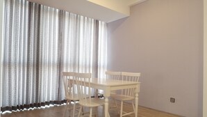 A room with a white table and four chairs, a large window with sheer curtains, and a light-colored wall. - 2BR Apartment near Marvell City Mall at The Linden (Surabaya)