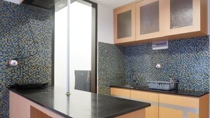 A kitchen with a black countertop, wooden cabinets, and a tiled backsplash. - 2BR Apartment near Marvell City Mall at The Linden (Surabaya)