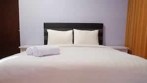 A neatly made bed with white linens and pillows, a dark headboard, and a white nightstand with a rolled white towel. - 2BR Apartment near Marvell City Mall at The Linden (Surabaya)