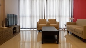 A modern living room with a flat-screen TV, two armchairs, a sofa, a coffee table, and a large window with sheer curtains. - 2BR Apartment near Marvell City Mall at The Linden (Surabaya)